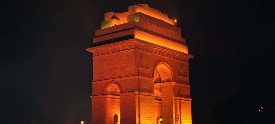 "India Gate illuminated at night with orange and yellow lights"