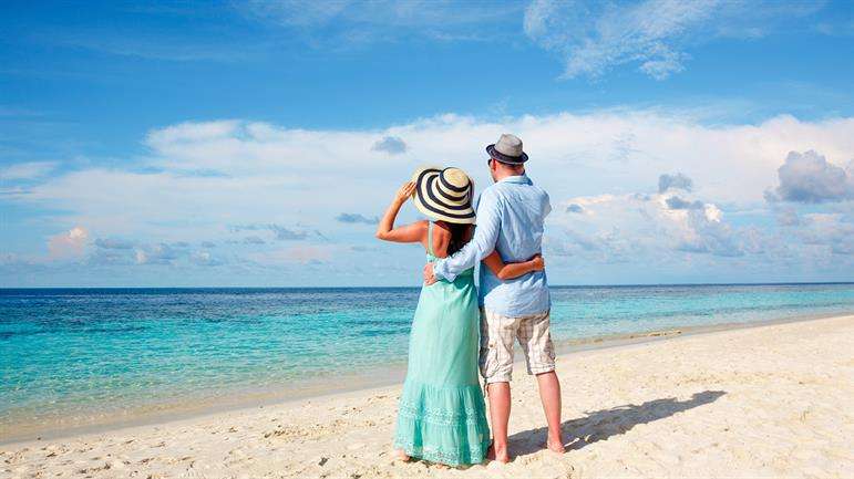 "Honeymoon couple walking hand in hand on a tropical Sri Lankan beach with crystal clear waters and blue sky."