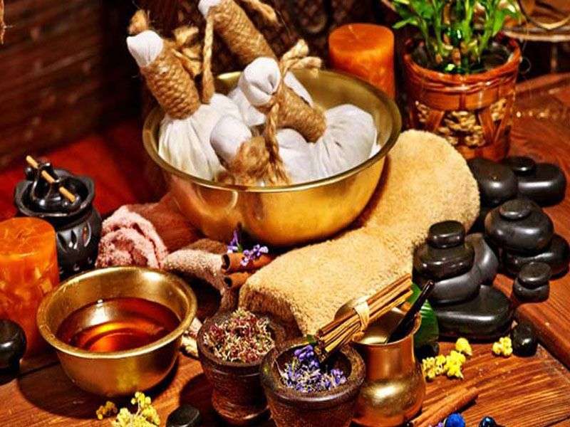 Ayurveda massage preparation items such as lentils, black stones, incense sticks, and oil arranged on a table.