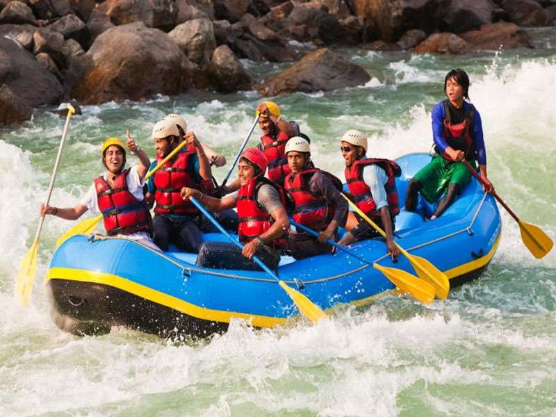 Tourists wearing life jackets and helmets, enjoying river rafting in Rishikesh, surrounded by beautiful natural scenery.