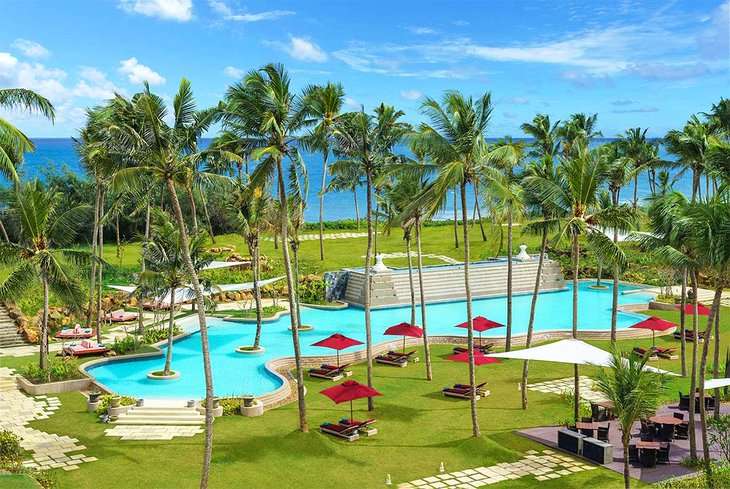 A view of the Shangri-La Hambantota Golf Resort & Spa located on a pristine beach in Sri Lanka, with palm trees, blue sky, and turquoise water in the background.