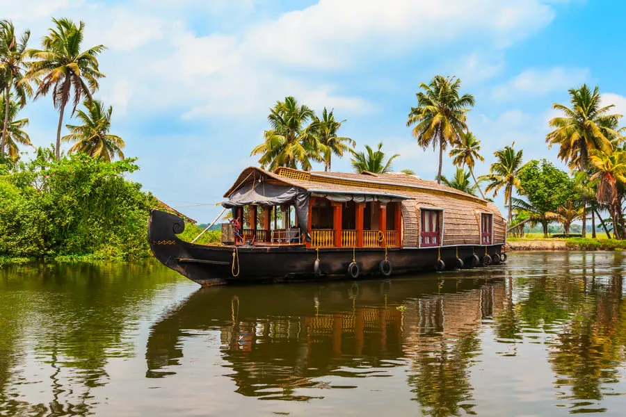 "A traditional houseboat floating on the serene waters of Kerala's backwaters, surrounded by lush greenery."