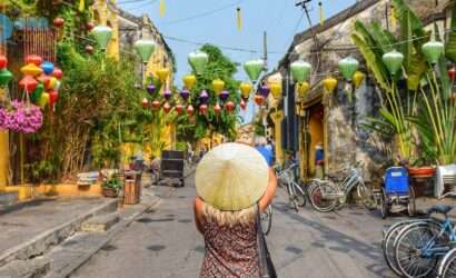 "A woman wearing a Vietnam cap stands on a street decorated with hanging lanterns."