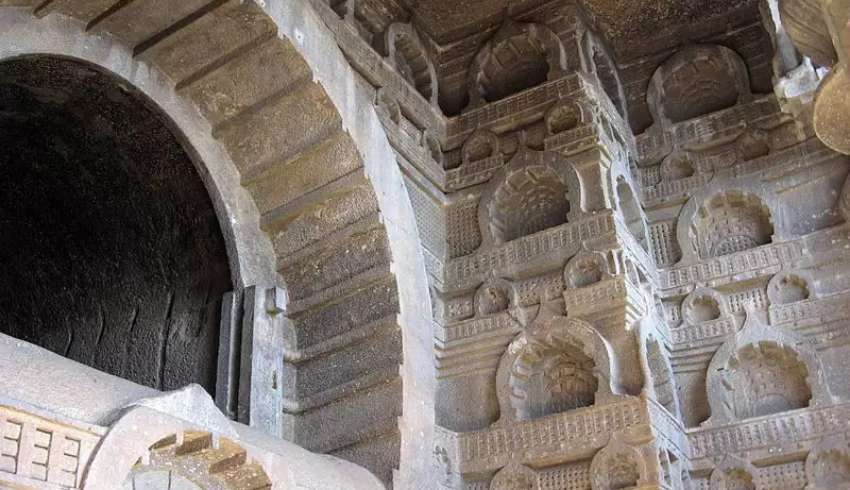 "An interior view of the rock-cut Bedse Caves in Kamshet, Maharashtra, India, showcasing intricate carvings and sculptures on the walls."