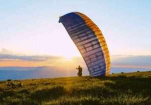 A person paragliding over lush green hills in Kamshet, with blue sky and white clouds in the background."